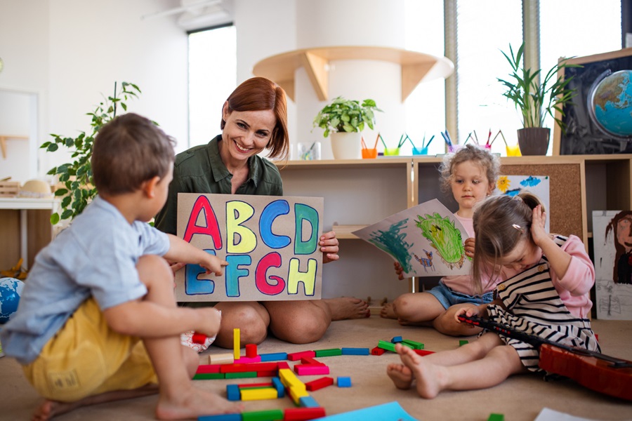 Group of small nursery school children with teacher on floor indoors in classroom, learning.