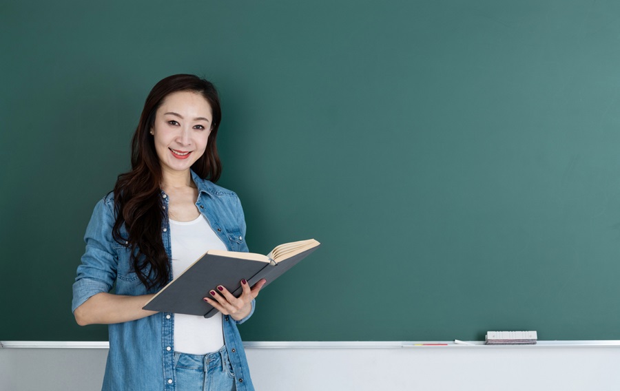 teacher holding book in front of blackboard